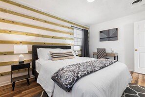 Een netjes opgemaakt slaapkamer met een bed, nachtkastjes, een lamp en een kunstwerk aan de muur.