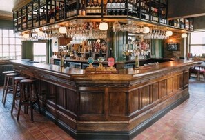A bar area with a wooden bar counter, stools, and a variety of bottles and glasses on shelves. - Historic Wing in Tring: Cozy and Scenic (Hertfordshire)