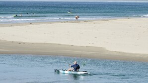 En strand med en person i en lille båd i vandet, sandstrand og et bjerg i baggrunden.