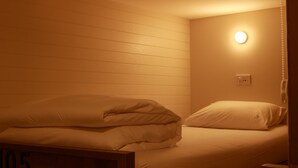 A single bed with white bedding in a room with white walls and a single light fixture on the wall. - Shanti Hostel  (Chiang Mai)