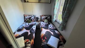 Een kamer met twee bedden, elk voorzien van beddengoed met pandabeeldjes, een plank met spullen en een raam met gordijnen.