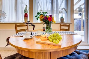 A round wooden dining table with a white tablecloth, a vase of flowers, a cheese board with grapes, and a coffee maker. - Cozy twin bed Studio- North London- free parking (London)