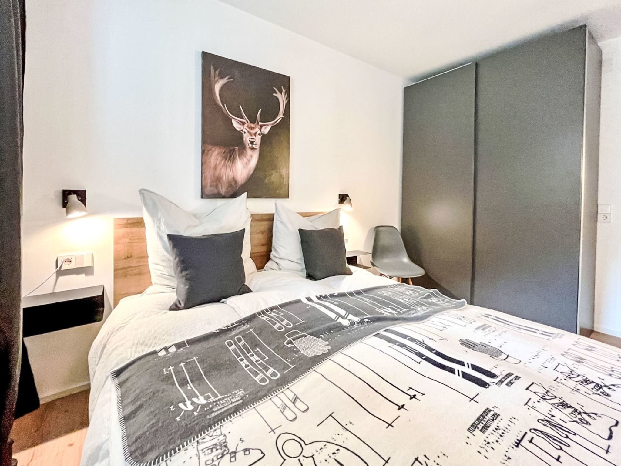 A modern bedroom with a large bed, a deer's artwork on the wall, and a wardrobe.