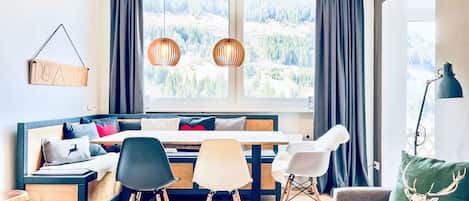 Un salon moderne comprenant un canapé, une table à manger et des chaises. Une fenêtre offre une vue sur une forêt.
