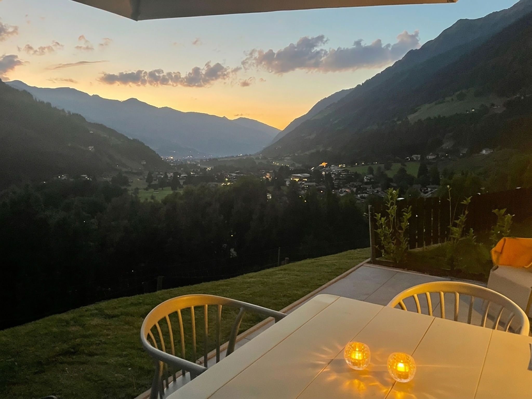 A terrace with a table and chairs overlooking a valley with mountains and a town.