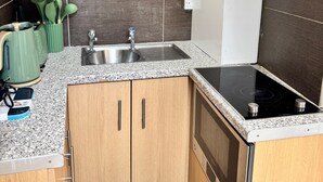 A kitchen with a granite countertop, stainless steel sink, and a black induction cooktop. - Eurostar Private Flat Sleeps up to 4 London (London)