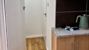 A narrow hallway with wooden flooring, a white door, and a kitchen area with wooden cabinets and a granite countertop. - Eurostar Private Flat Sleeps up to 4 London (London)
