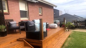 Een houten terras met buitenmeubilair, een bakstenen huis en een gazon.