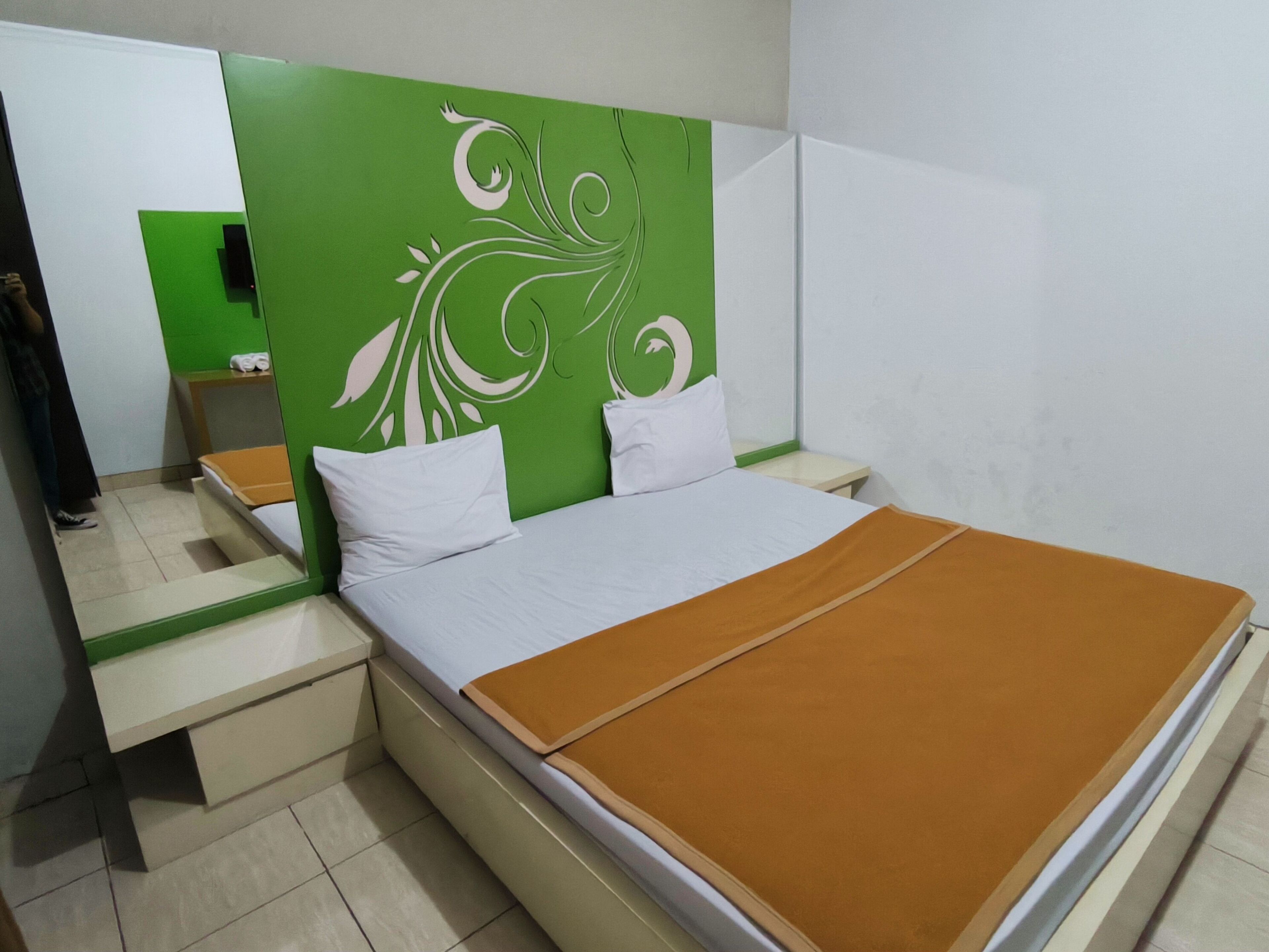 Une chambre d’hôtel avec un lit, une table de chevet, un miroir et un mur d’accent vert.