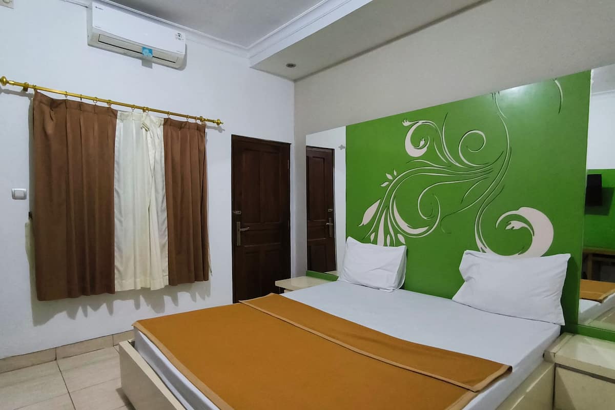 Una habitación de hotel con cama, mesita de noche, pared decorativa verde, ventana con cortinas y aire acondicionado.