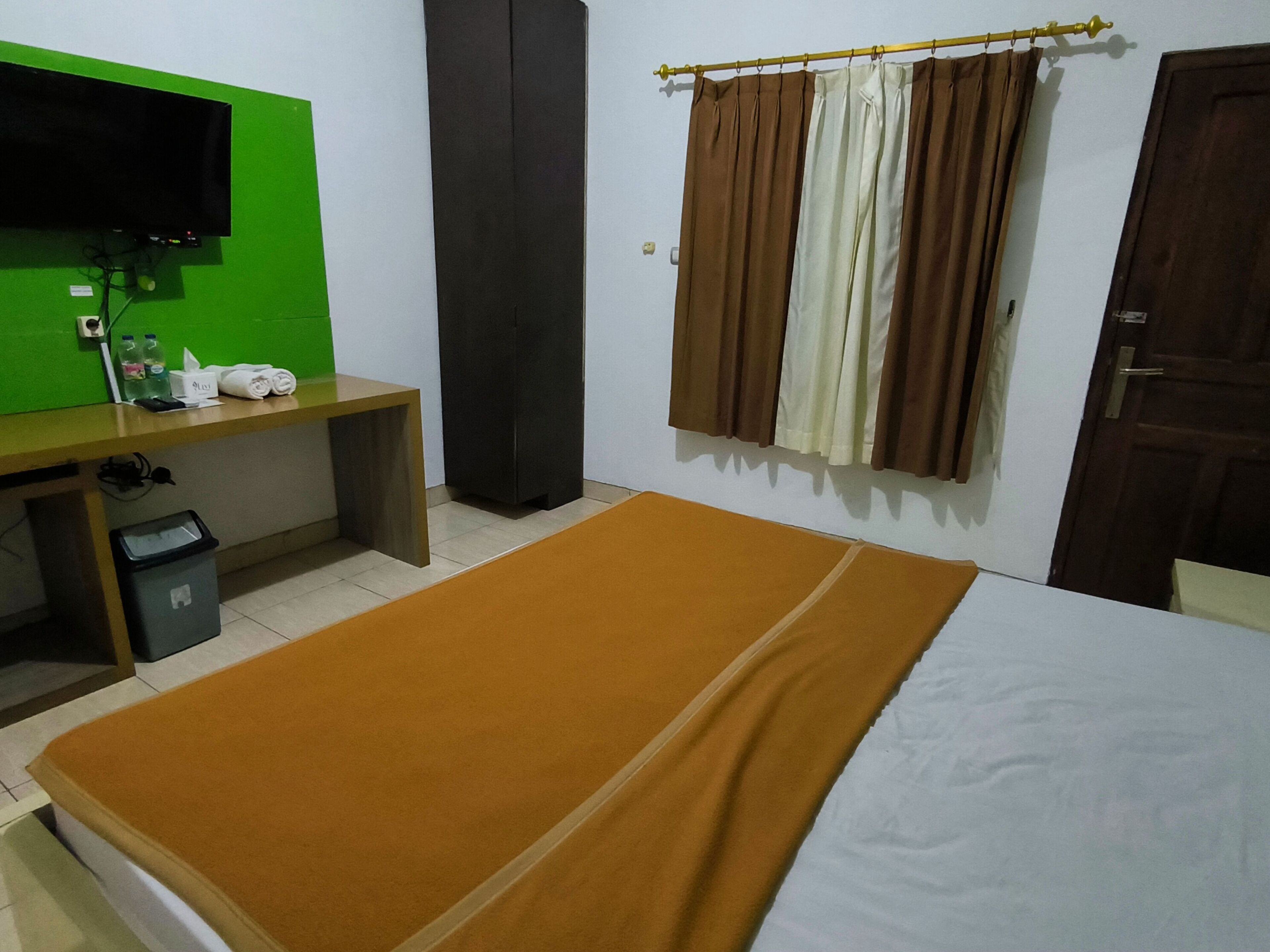 Quarto com cama, escrivaninha, televisão e guarda-roupa.