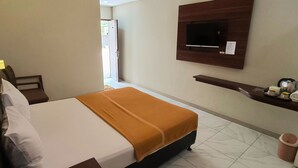 Una habitación de hotel con cama, televisor montado en la pared, un pequeño estante con artículos de aseo y un cesto de basura.
