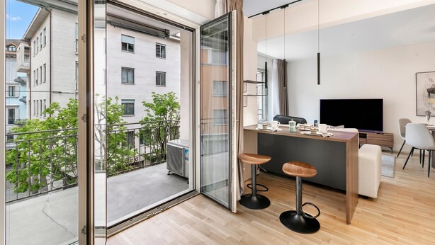 Un apartamento moderno con balcón, cocina y sala de estar con televisor.
