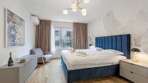 Un dormitorio moderno con una cama grande, una mesita de noche, una silla, un escritorio y una ventana con cortinas.