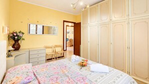 Ein Schlafzimmer mit Bett, Schminktisch, Spiegel, Kleiderschrank und einem kleinen Schreibtisch mit Lampe.