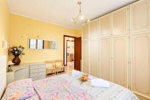Une chambre à coucher comprenant un lit, une commode, un miroir, une armoire et un petit bureau avec une lampe.