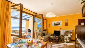 Ein Essbereich mit Esstisch für vier Personen, einer Couch, einem Fernseher und Blick durch ein großes Fenster.