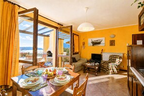 Un coin repas avec une table dressée pour quatre personnes, un canapé, un téléviseur et une vue dégagée sur l’extérieur grâce à une grande fenêtre.
