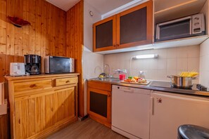 A compact kitchen with wooden cabinets, a microwave, a coffee maker, and a dishwasher.