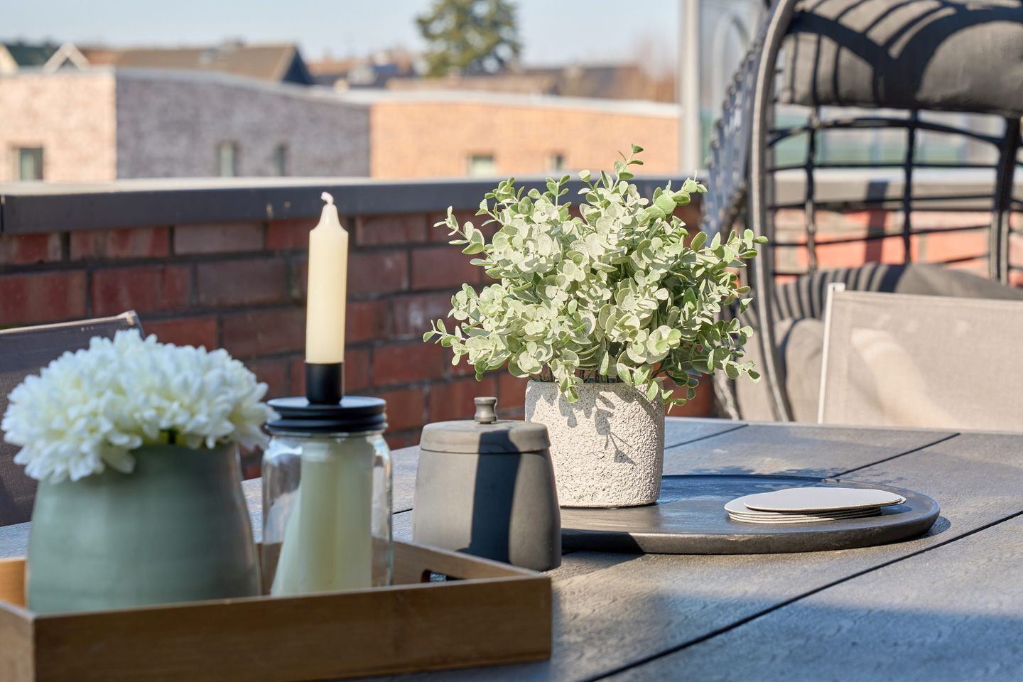 A table with a candle, a potted plant, and a jar of flowers on a rooftop terrace.