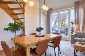 A modern living room with a wooden dining table, brown leather chairs, a grey sofa, and a staircase with wooden railings.