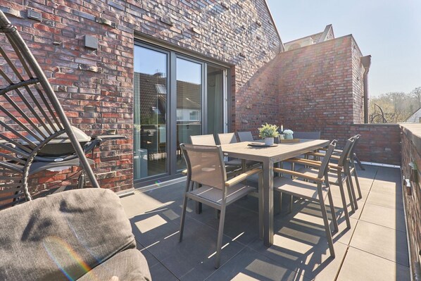 A patio with a table and chairs, a brick wall, and a sliding glass door.