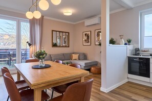 A modern living room with a wooden dining table, brown leather chairs, a grey sofa, and a kitchen area with a stove and cabinets.