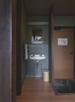 Un pasillo estrecho que conduce a un baño con un lavabo, un perchero para toallas y un cubo de basura.