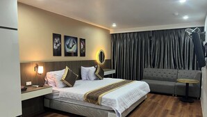 Una habitación de hotel moderna con una cama grande, un sofá gris, una mesita redonda y un espejo.
