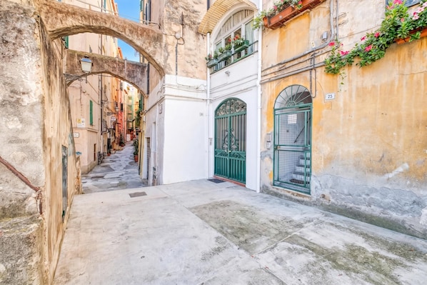 Una estrecha calle con un arco de piedra, un portón verde y un edificio con el número 25.
