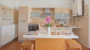 Ett modernt kök med en central köksö, träskåp, en inbyggd ugn och ett stort fönster ovanför diskbänken.