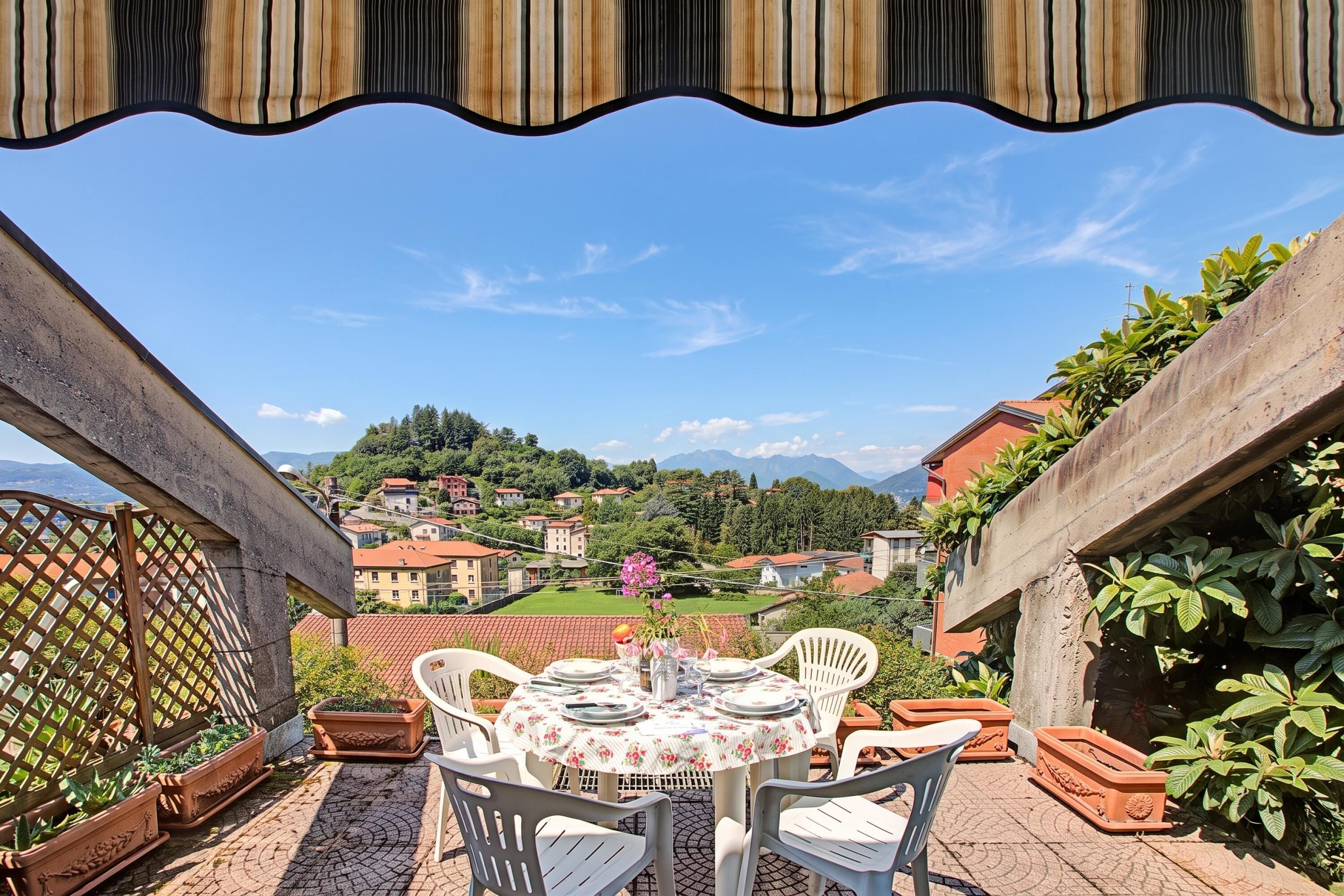Una terrazza con un tavolo apparecchiato per mangiare, con vista su un borgo collinare.