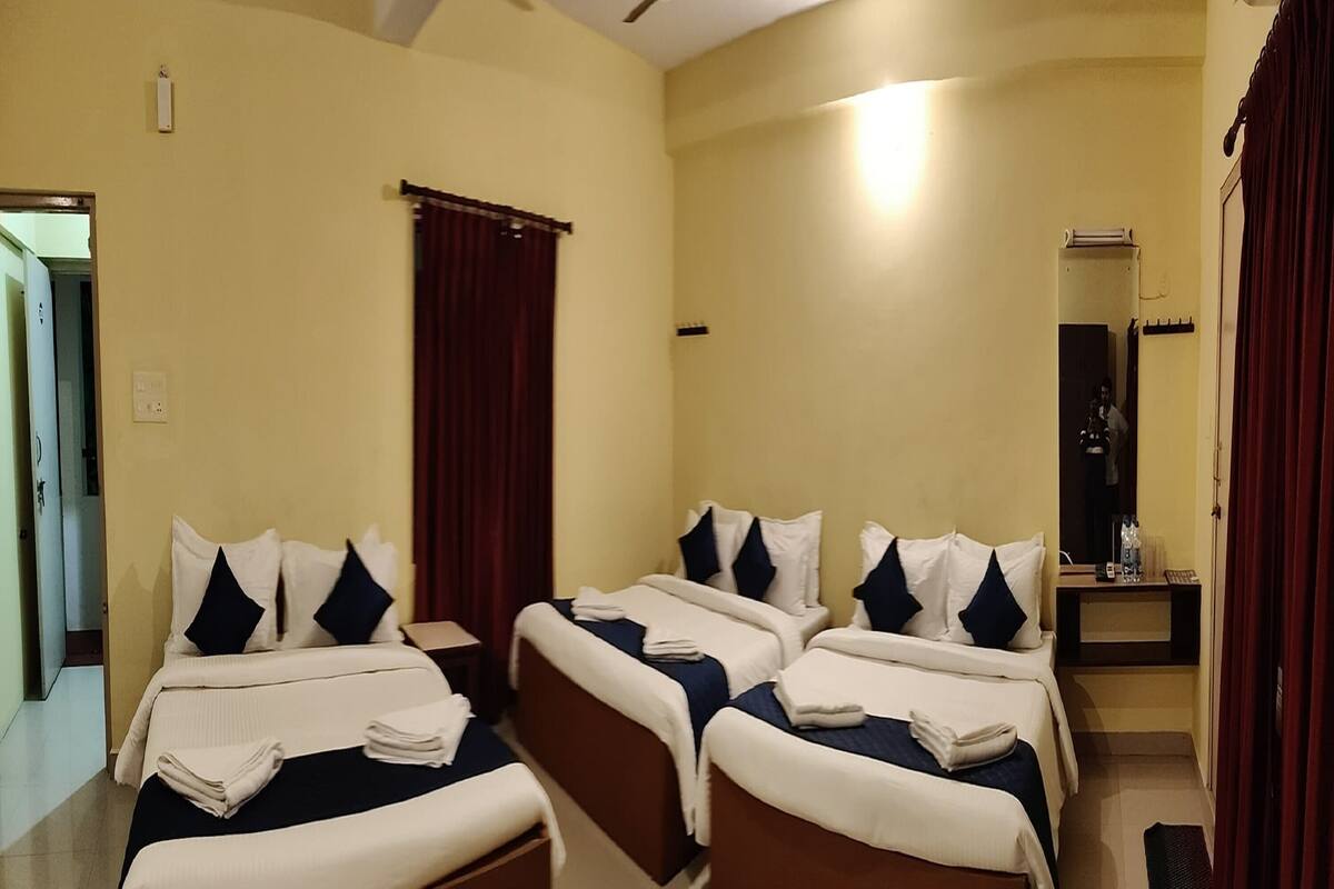 A hotel room with three beds arranged in a U-shape, a ceiling fan, and a small table with a mirror and a telephone.
