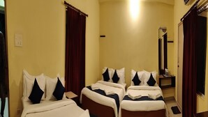A hotel room with three beds, each with white and navy bedding, and dark curtains. - Hotel Tenach (Puducherry)