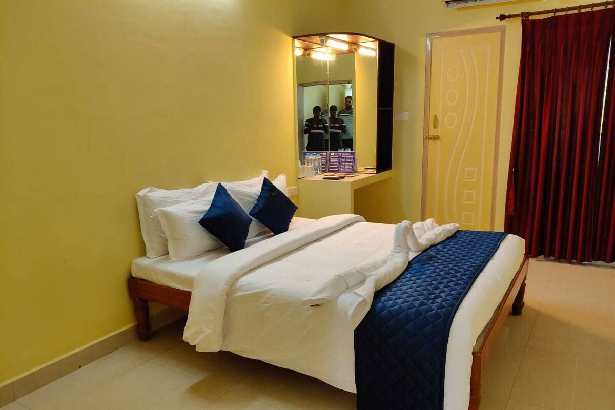A hotel room with a bed, a mirror, a wardrobe, and a red curtain.