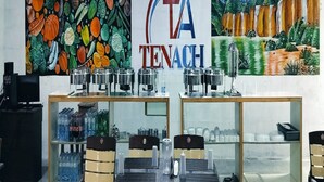 A restaurant interior with a mural of vegetables, a 'TA TENACH' sign, and a buffet setup. - Hotel Tenach (Puducherry)