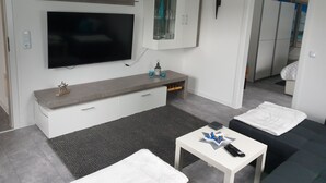 Una sala de estar moderna con un televisor de pantalla plana, un mueble con puertas de vidrio, una mesita con un control remoto y un sofá.