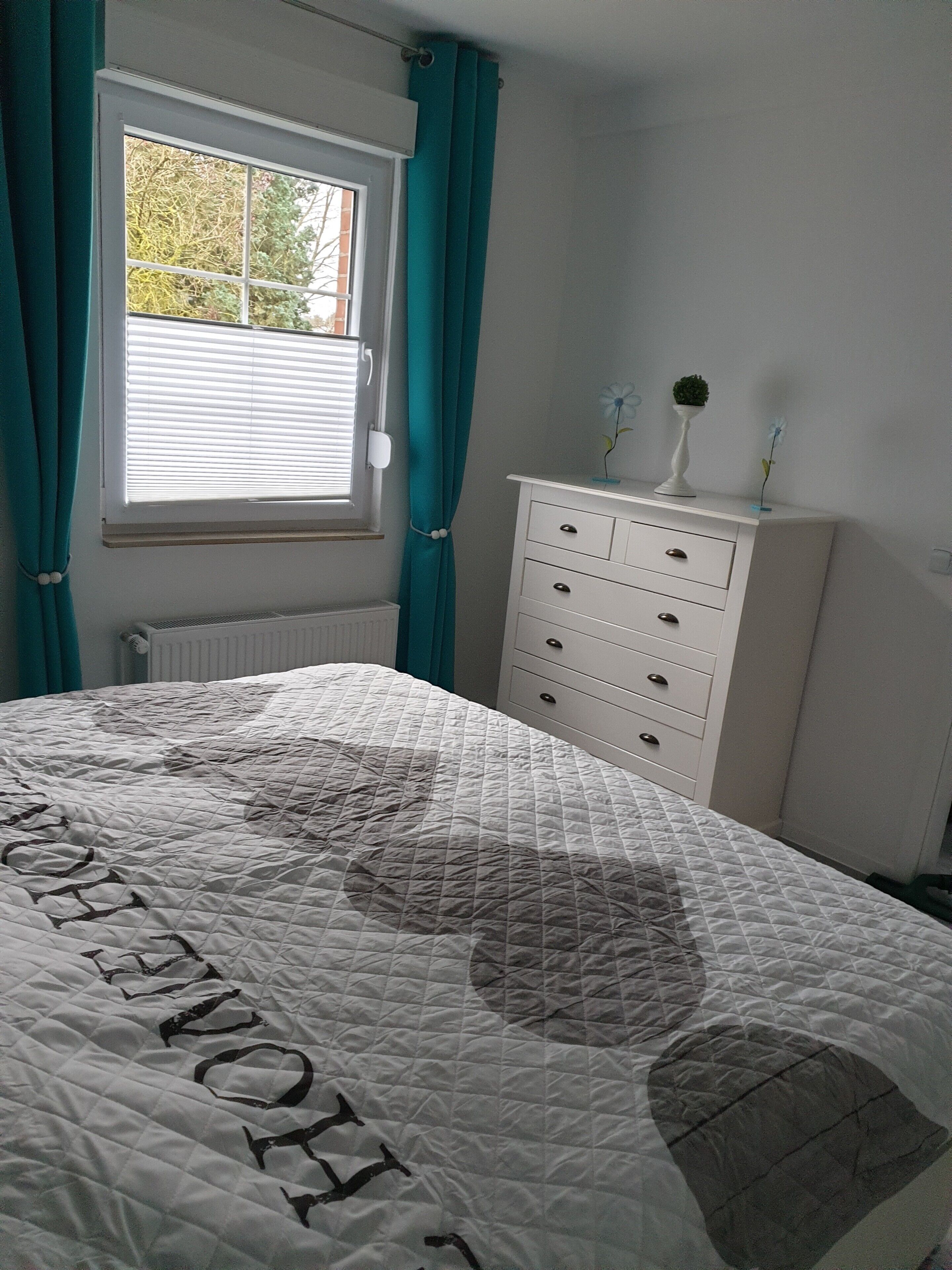 Un dormitorio con cama, cómoda, ventana con cortinas y radiador.