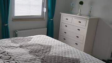Un dormitorio con cama, cómoda, ventana con cortinas y radiador.