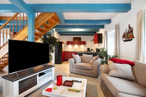 Een woonkamer met een flatscreen televisie, een bank, een salontafel met afstandsbedieningen en een trap met houten leuningen.