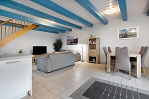 A modern living room with a sofa, TV, and dining area with chairs. - Apartment "Vogelkoje" with Private Terrace, Shared Garden and Wi-Fi (Pellworm)
