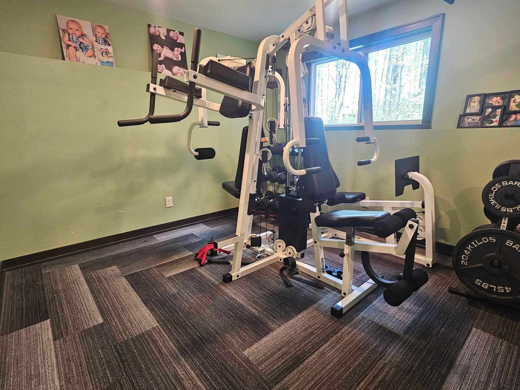 A gym with a multi-functional workout machine, weight racks, and a window providing natural light.