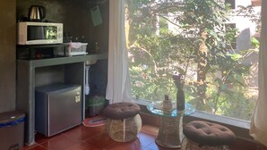 Cozinha compacta com micro-ondas, frigorífico e uma pia pequena. Há uma janela com vista para um jardim verde e uma árvore.