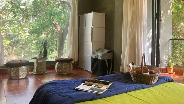 Quarto com cama, janela com cortinas, radiador e vista para o verde lá fora.