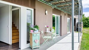 A covered outdoor area with a wooden staircase, a small table with chairs, and a cabinet with a heart-shaped decoration. - Room 'Doppelzimmer' with Private Terrace, Shared Garden and Wi-Fi (Leibertingen)