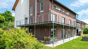 A modern two-story building with a balcony, outdoor seating, and a garden area. - Room 'Doppelzimmer' with Private Terrace, Shared Garden and Wi-Fi (Leibertingen)