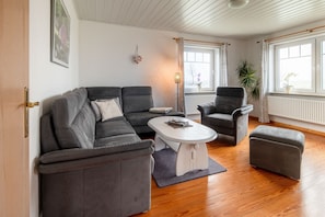 A modern living room with a grey sofa, a white coffee table, and a grey armchair.