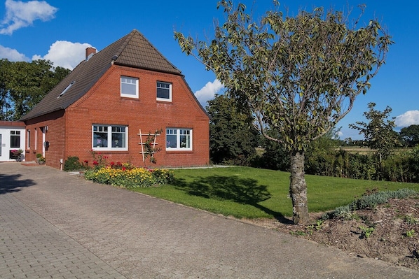 A red brick house with a sloped roof, a front porch, and a well-maintained lawn.
