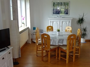 A dining area with a round table, wooden chairs, a TV, and a fireplace.