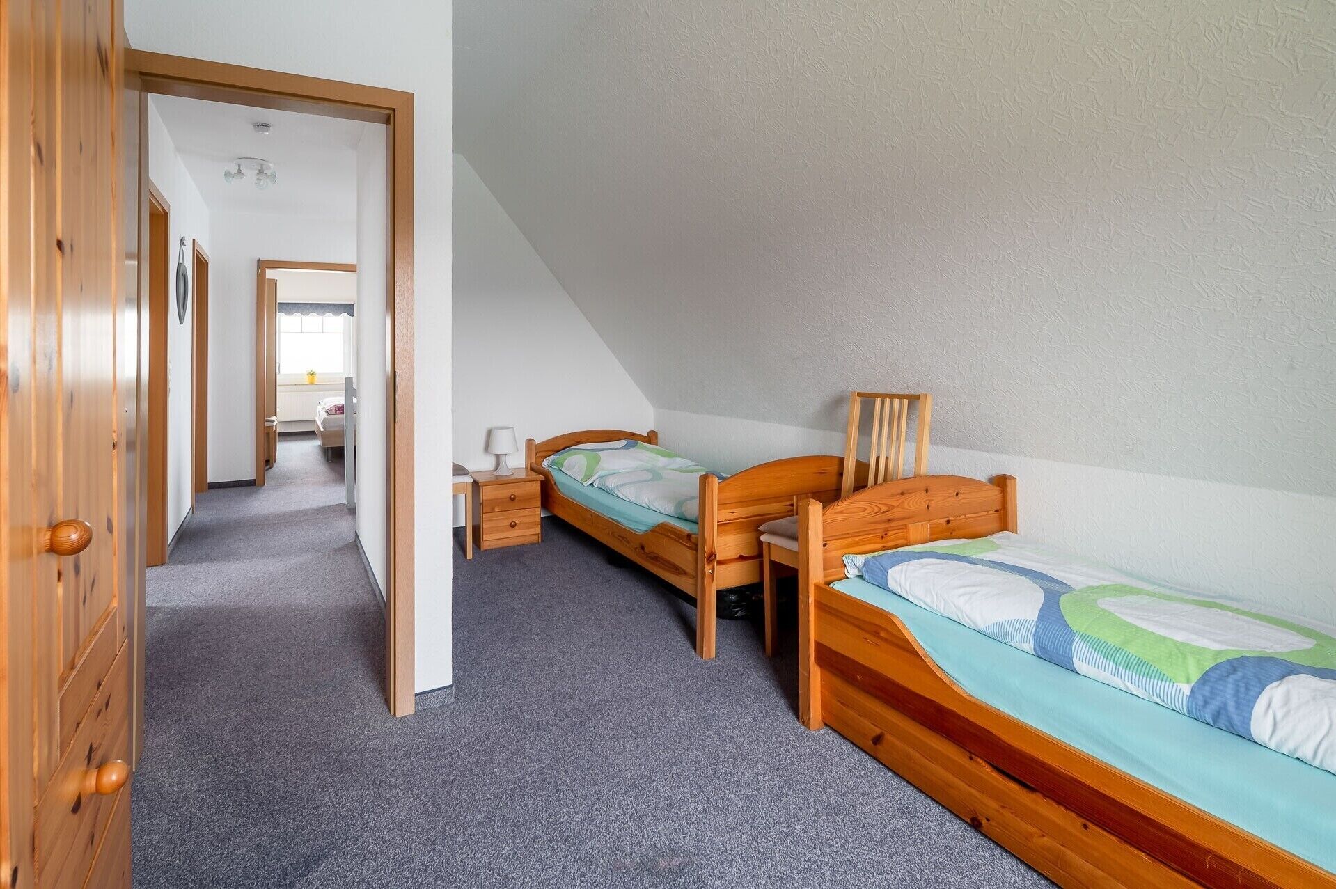 A bedroom with two wooden beds, a desk, and a chair.